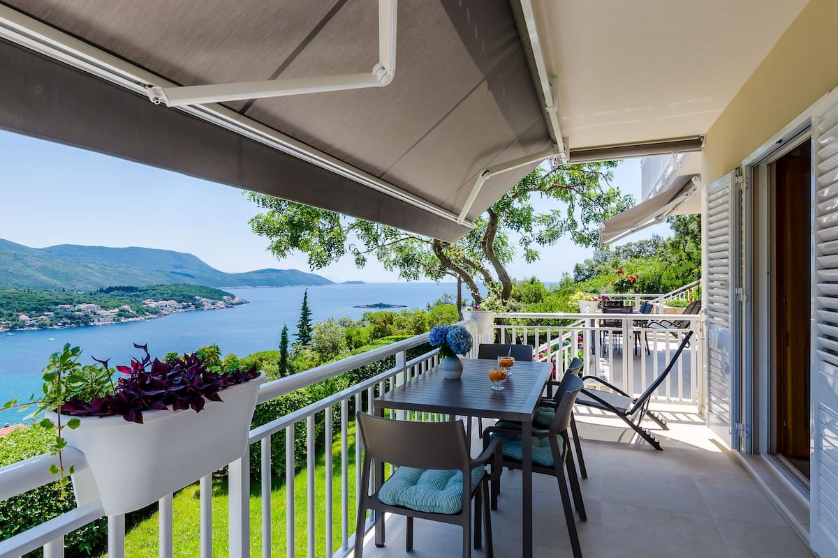 A balcony with a table and chairs, overlooking a lake and mountains.