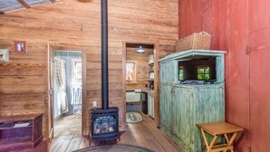 A rustic cabin interior with a wood-burning stove, a television on a cabinet, and a small wooden stool. - Ada's Whole House 3 Bedroom Apts by RedAwning (Fredericksburg)
