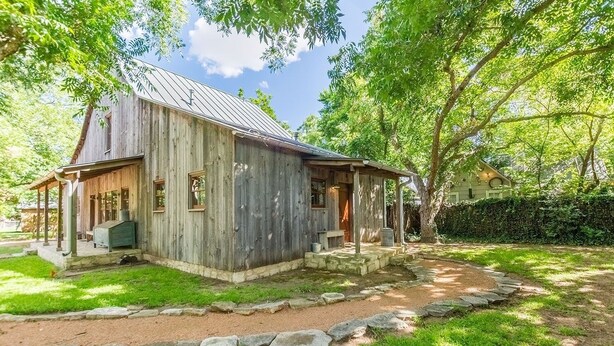 A rustic wooden cabin with a porch, surrounded by lush greenery and a stone pathway. - Ada's Whole House 3 Bedroom Apts by RedAwning (Fredericksburg)