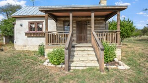 Une cabane rustique en rondins de bois, dotée d’un porche en bois, d’un escalier en pierre et d’un toit en métal.