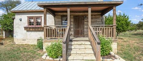 A rustic log cabin with a wooden porch, stone steps, and a metal roof.