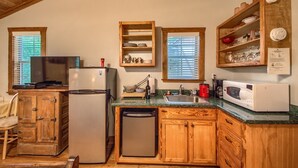 A kitchen with wooden cabinets, a refrigerator, a microwave, and a sink. - Waldrip Studio Bedroom Cabin by RedAwning (Fredericksburg)