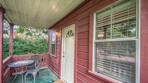 A porch with a red wooden house, a white door, and a window with blinds. - Waldrip Studio Bedroom Cabin by RedAwning (Fredericksburg)