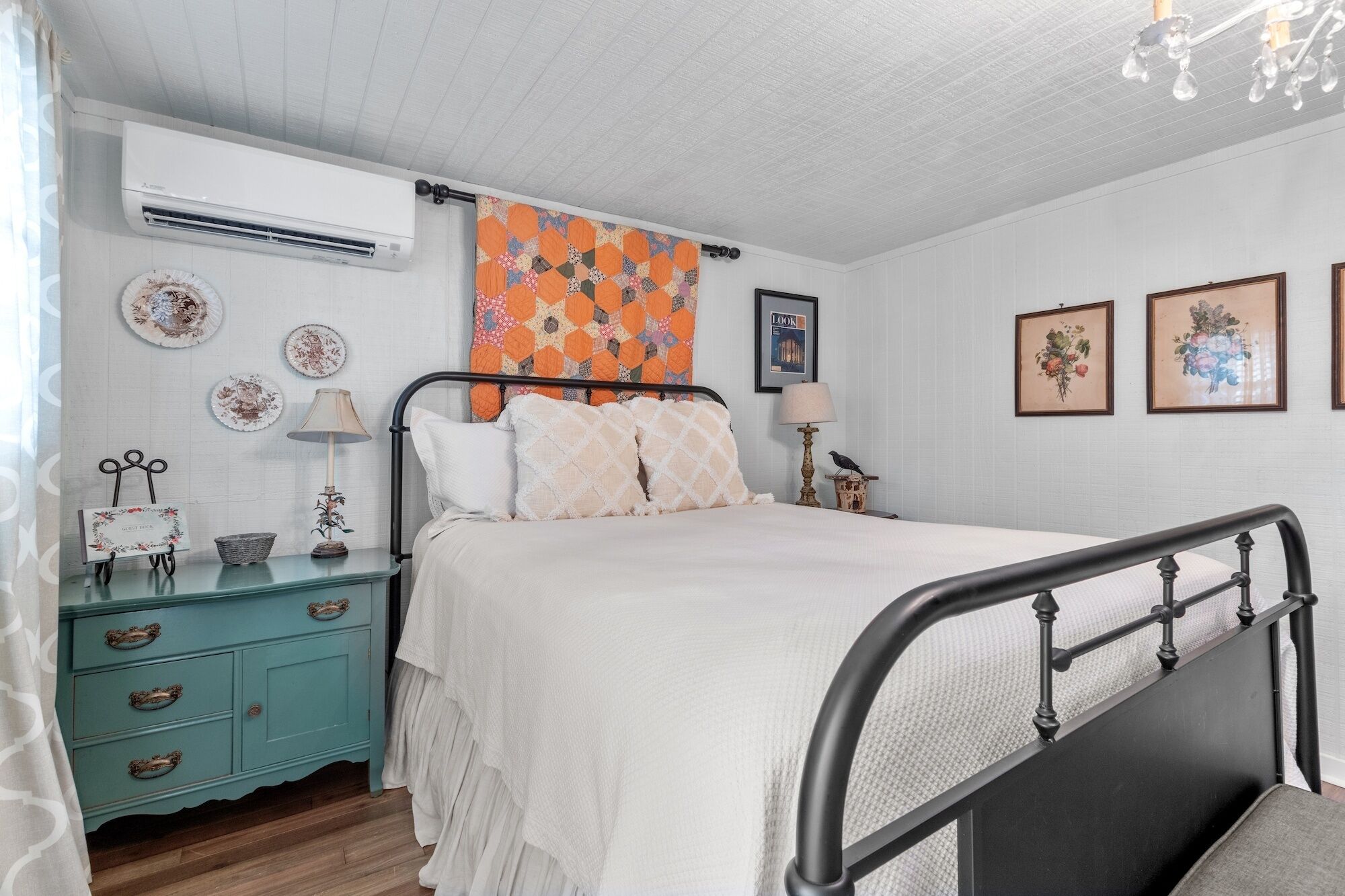 A bedroom with a bed, a nightstand, a dresser, and a window with a patterned curtain.