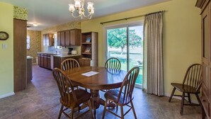 A dining area with a wooden table and chairs, a chandelier, and a view of a garden through large windows. - Oma's Haus 2 Bedroom Home by RedAwning (Fredericksburg)