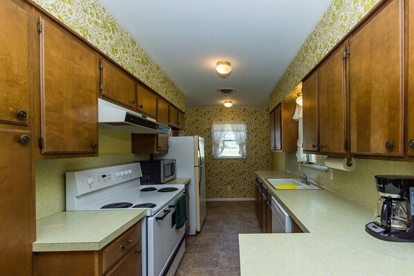 A compact kitchen with wooden cabinets, a white stove, a microwave, and a coffee maker.