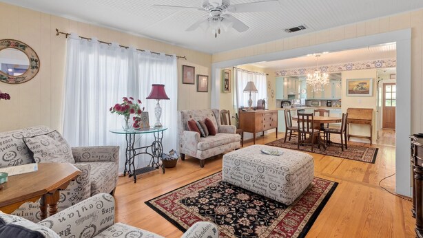 A spacious living room with a ceiling fan, a dining area with a chandelier, and a kitchen visible through an open doorway. - Das Bierschwale Gastehaus 2 Bedroom Home by RedAwning (Fredericksburg)