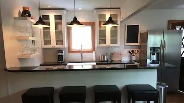 A modern kitchen with a central island, bar stools, and pendant lighting. - Beautiful 5-bedroom cottage across from Bass Lake (Pentwater)