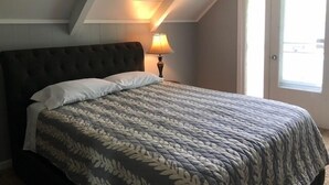 A bedroom with a dark headboard, a bed with a patterned bedspread, a bedside lamp, and a door with a view to the outside. - Beautiful 5-bedroom cottage across from Bass Lake (Pentwater)