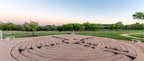 A circular labyrinth on a paved area with benches and trees in the background.