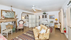 A spacious living room with a fireplace, a ceiling fan, and a dining area with a table and chairs. - Binky's Summer Afternoon Studio Bedroom Cottage by RedAwning (Fredericksburg)