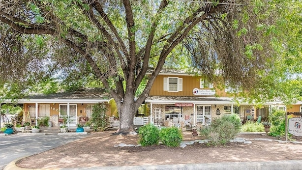 A two-story building with a porch, a sign indicating 'Austin Street' and 'Moffin House', and a large tree in front. - Binky's Summer Afternoon Studio Bedroom Cottage by RedAwning (Fredericksburg)