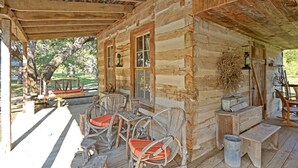 A rustic wooden cabin with a porch featuring wicker chairs with red cushions, a wooden table, and a hanging light fixture.