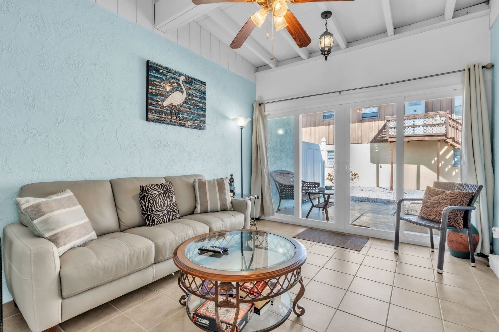 A living room with a beige sofa, a glass coffee table, and a view of an outdoor deck through glass doors.