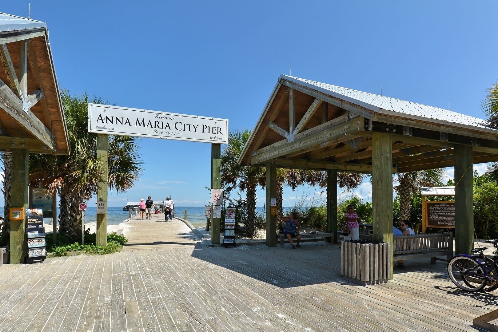 Un muelle con un cartel que indica Muelle de Anna Maria, una tienda de recuerdos y vista a la playa.