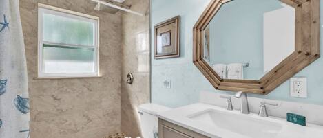 A bathroom with a shower, a sink, a toilet, and a large mirror.