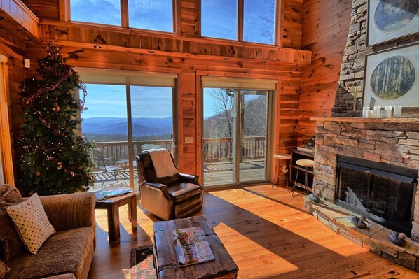A log cabin interior with a fireplace, a Christmas tree, a leather chair, and a sofa.