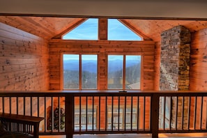 A wooden cabin with a balcony, large windows, and a stone fireplace. - Sky High in West Jefferson, NC: Spacious 4BR cabin for 10 with stunning mountain views. (West Jefferson)