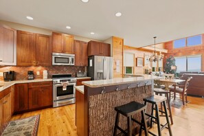 A modern kitchen with wooden cabinets, stainless steel appliances, a large island with bar stools, and a view of the outdoors.