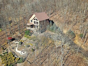 A two-story house with a balcony, surrounded by trees and a stone pathway.