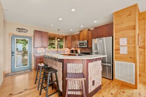 A modern kitchen with wooden cabinets, stainless steel appliances, and a central island with stools. - Sky High in West Jefferson, NC: Spacious 4BR cabin for 10 with stunning mountain views. (West Jefferson)
