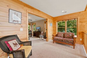 A cozy wooden interior with a sofa, a wicker chair, and a television in the background.
