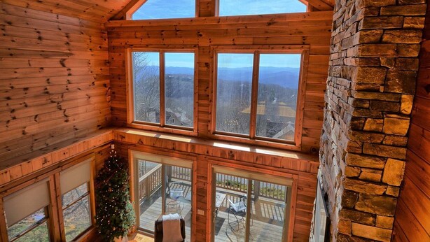 A cabin with a loft bedroom, large windows, a stone fireplace, and a Christmas tree. - Sky High in West Jefferson, NC: Spacious 4BR cabin for 10 with stunning mountain views. (West Jefferson)