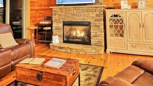 A cozy living room with a stone fireplace, leather furniture, and a television mounted above it. - Sky High in West Jefferson, NC: Spacious 4BR cabin for 10 with stunning mountain views. (West Jefferson)