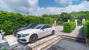 Une voiture blanche est garée dans une allée, un chemin de pierres menant à une entrée fermée par un portail.