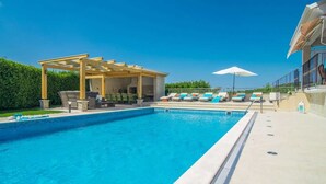 Une piscine dotée d’un espace de repos couvert, de chaises longues et de parasols.