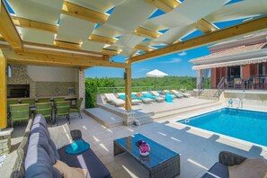 An outdoor pool area with lounge chairs, a barbecue, and a stone fireplace. - Villa Maklavun (Kanfanar)