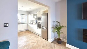 Une cuisine moderne avec des meubles blancs, des appareils en acier inoxydable et un parquet en bois disposé en motif chevron.