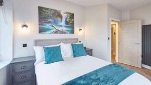 Une chambre à coucher comprenant un lit, une table de chevet, une commode, une lampe fixée au mur et une porte.