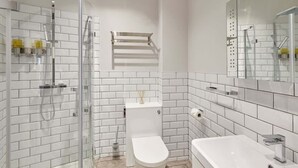 Une salle de bain moderne avec une douche à parois de verre, des toilettes blanches et un grand lavabo surmonté d’un miroir.