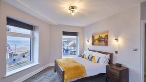 Una camera da letto con un'ampia finestra, un letto con una coperta gialla, un comodino e un quadro appeso alla parete.