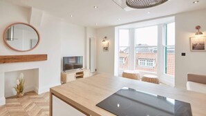 A modern kitchen with a built-in stove, a TV, and a large window with a view of buildings. - Host & Stay | Abbey Hus (Whitby)