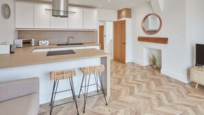 A modern kitchen with white cabinets, a stainless steel range hood, and a herringbone wood floor. - Host & Stay | Abbey Hus (Whitby)
