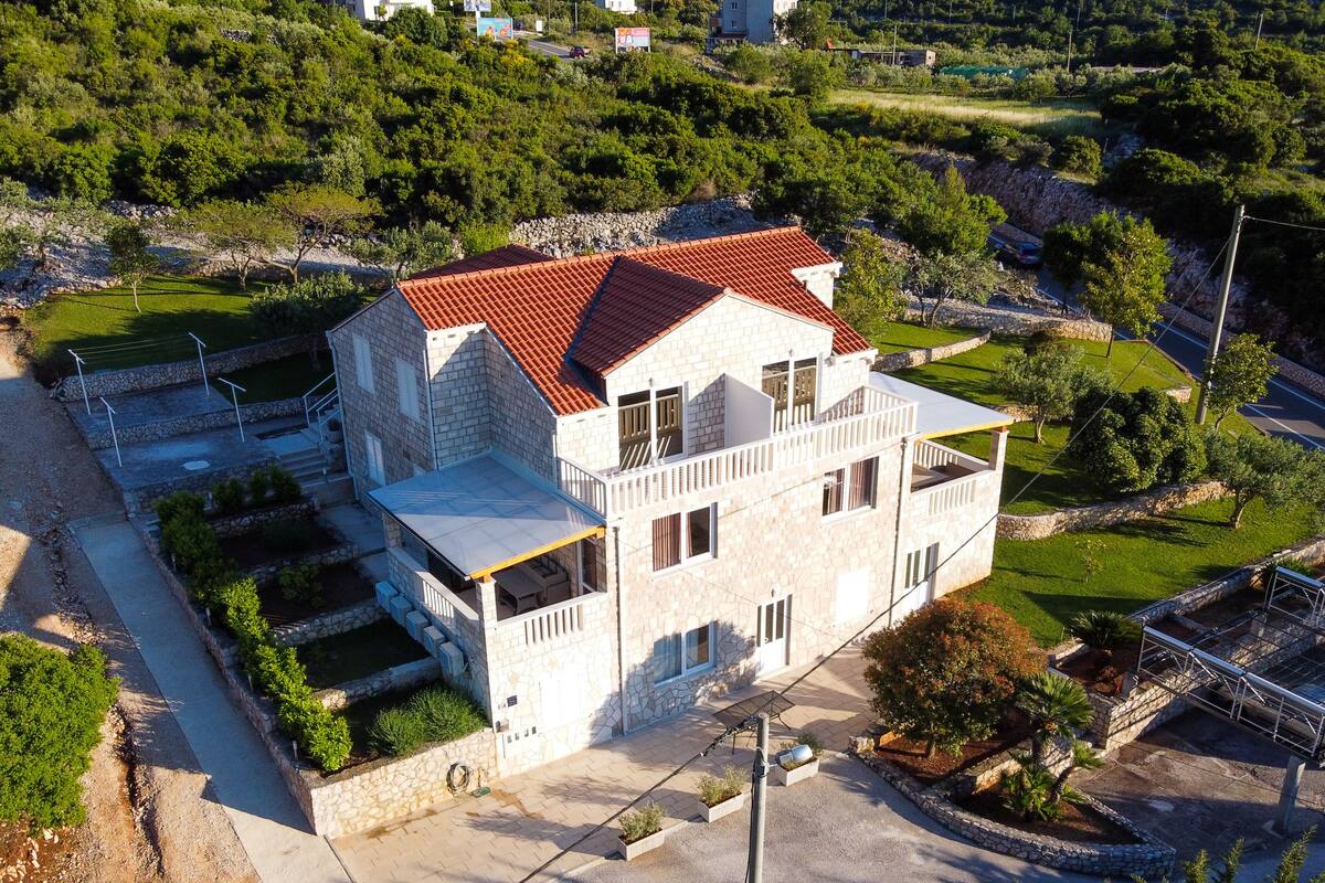 A two-story stone house with a red-tiled roof, a balcony, and a paved driveway.