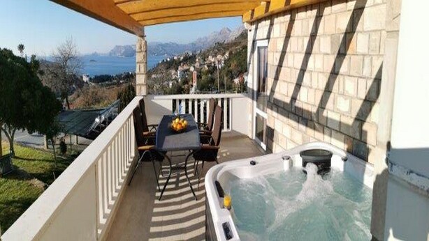 A balcony with a hot tub, a table with chairs, and a view of the mountains and sea.