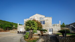 A two-story stone house with a balcony, a stone staircase, and a well-maintained garden.