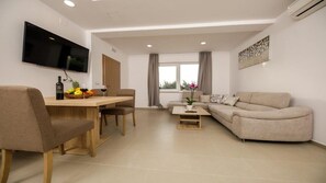 A modern living room with a dining area, a flat-screen TV mounted on the wall, a sofa, and a coffee table. - Apartments Mi&ni (Konavle)