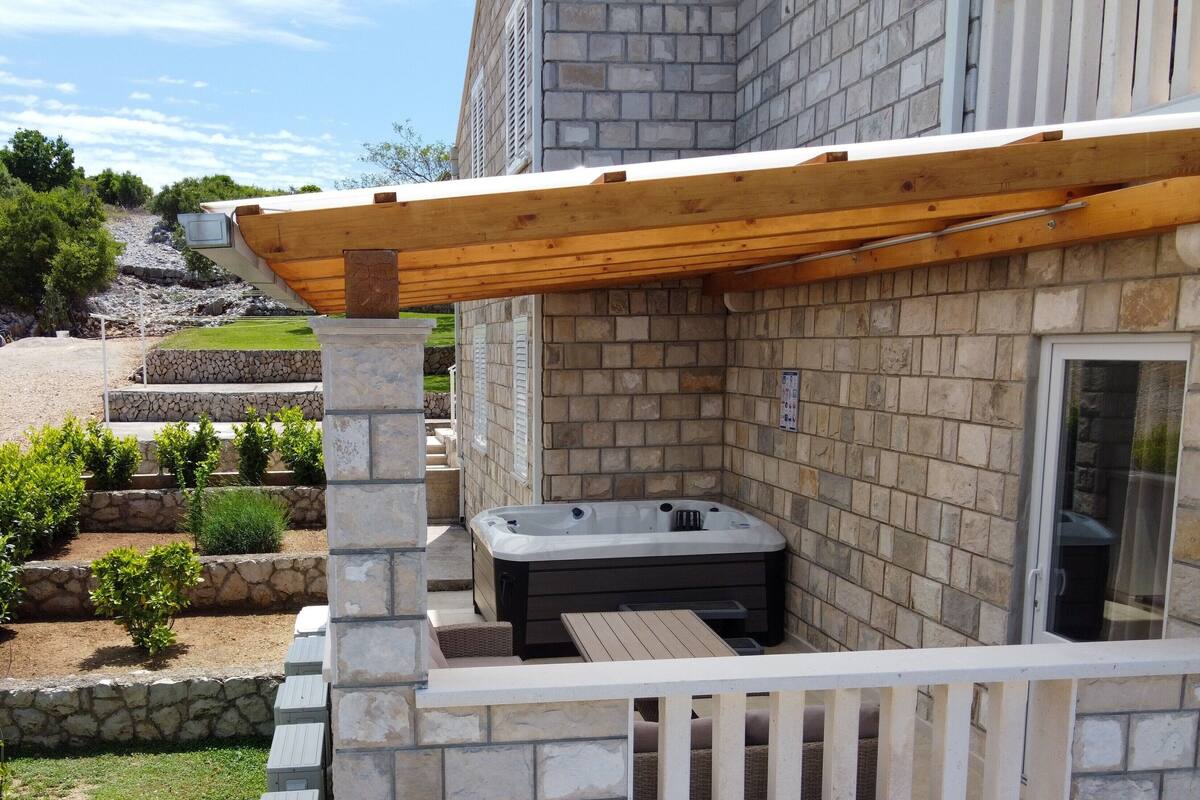 A stone exterior with a wooden pergola and a hot tub.