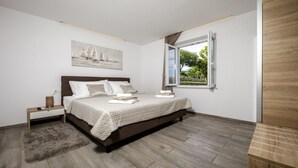 A bedroom with a bed, a bedside table, a nightstand, a window with a view, and a painting on the wall.
