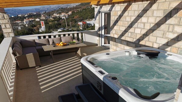 A balcony with a hot tub, a sofa, and a table with fruits and a bottle. - Apartments Mi&ni (Konavle)