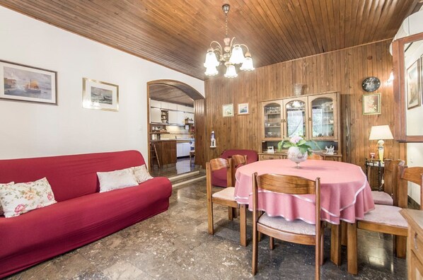 A cozy living room with a red sofa, wooden dining table with pink tablecloth, and a chandelier.