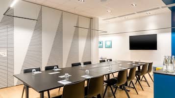 A conference room with a long table, chairs, a flat-screen TV, and a blue accent wall.