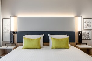 Quarto de hotel com uma cama grande, duas mesas de cabeceira e cabeceira com iluminação embutida.