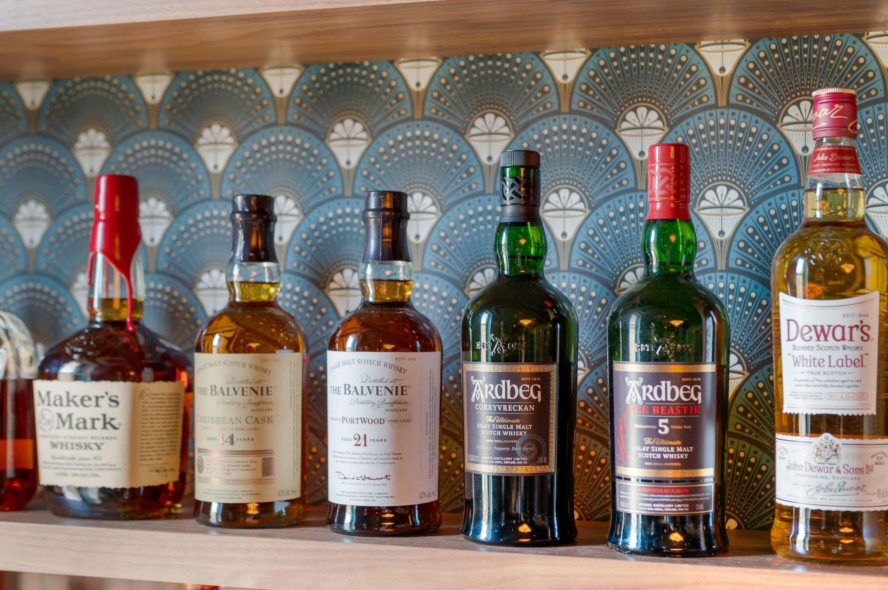 A row of whisky bottles on a shelf against a patterned tile wall.
