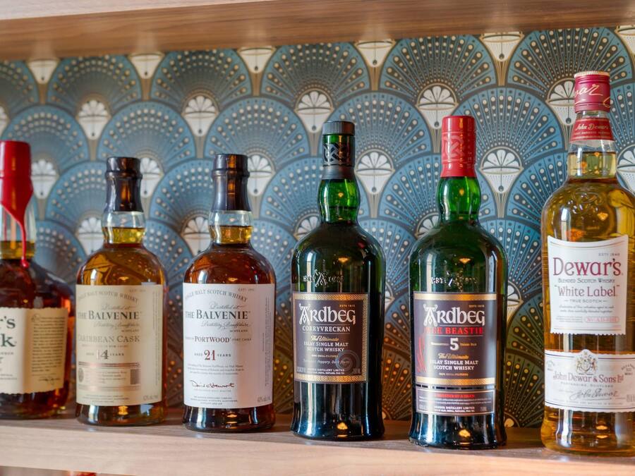 A row of whisky bottles on a shelf against a patterned tile wall.