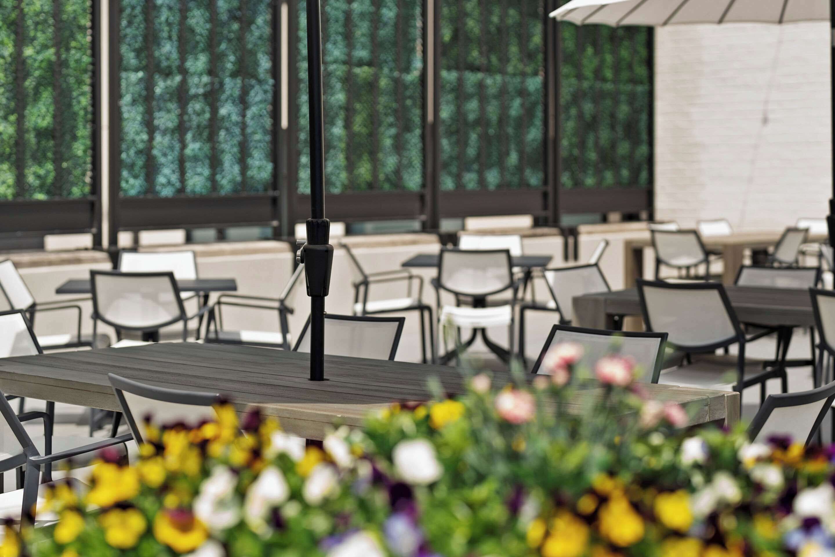 An outdoor seating area with tables and chairs, surrounded by a garden with various flowers.